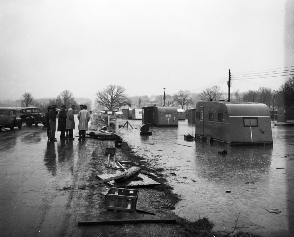 Flood at the University of Wisconsin-Madison East Hill Trailer Camp, located at 451 North Midvale Boulevard, south of University Avenue. Several men are shown standing on Midvale Boulevard observing the flood waters surrounding several mobile homes.