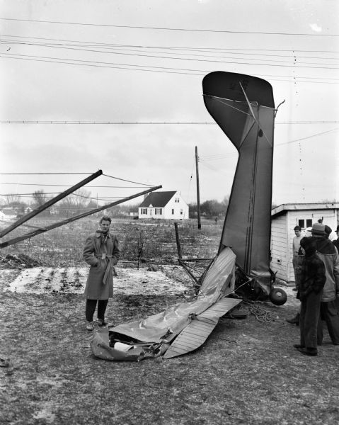 View of small private plane which crashed into a 30-foot open space narrowly missing the home of Mr. and Mrs. John Vick at 102 Lansing Street and an adjacent home. Two World War II veteran brothers-in-law, David E. Hill and Robert L. Horstmeyer, were pinned in the cockpit.  David Hill, the pilot, was killed and his brother-in-law was seriously injured. Looking at the wreckage is Connie Elver, 14, of 104 Lansing Street, whose bedroom was nearly struck by the nose-diving airplane.