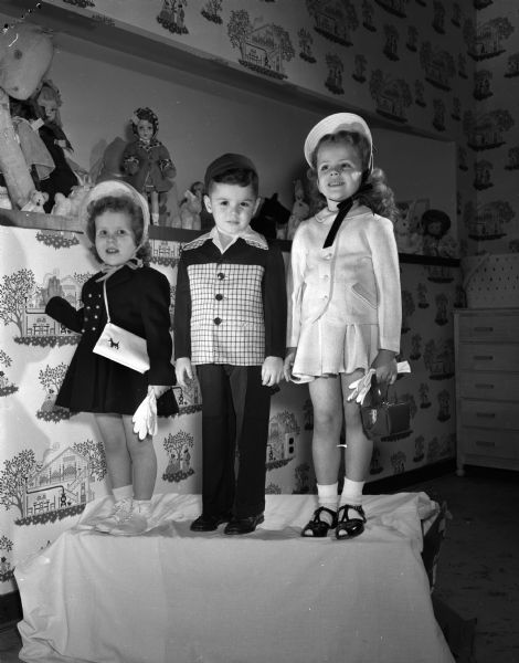 Susan Severson, Michael Wonn, and Sheila Nygaard model their spring outfits in front of a display of dolls.