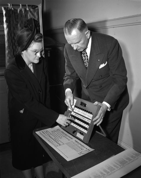 First Step: The voter (Mrs. Thelma Hauser) receives her first instructions from the election official (Arvid Johnson) on a small working model.  She must operate it herself to show that she understands.