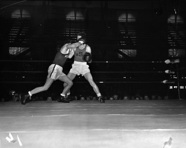 University of Wisconsin boxer John Lendenski, left, landing a right punch to the head of Syracuse University boxer Julian LeVine, who is preparing to retaliate with a left punch. The two men are participating in the NCAA championship being held at the University of Wisconsin-Madison Field House. The heads of the crowd can be seen in the background.