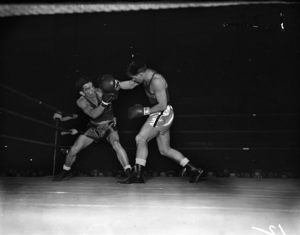 California Aggies' Don Brown has just blocked a right hand smash by the Badgers' Don Dickinson in the first round of their light heavyweight bout. The two men are participating in the NCAA championship being held at the University of Wisconsin-Madison Field House.