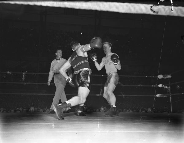 Eddie Rieder of Maryland is throwing a sweeping right to the jaw of Idaho's Herb Carlson in their middleweight bout. Referee B.J. Barrodale is the third man in the ring. The two men are participating in the NCAA championship being held at the University of Wisconsin-Madison Field House.