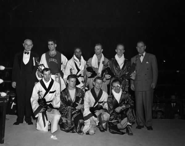Group portrait of eight NCAA boxing tournament champions who advanced to the Olympic boxing team trials. Back row, L to R: Dr. Carl Schott, Penn State, co-manager of the Olympic team; Vito Parisi, Wisconsin heavyweight; Calvin Vernon, Wisconsin light heavyweight; Herb Carlson, Idaho, middleweight; Charles Davey, Michigan State, lightweight and John J. Walsh, Wisconsin, co-coach of the Olympic team. Front row, L to R: Don Dickinson, Wisconsin, welterweight; Douglas Ellwood, Louisiana State, featherweight; Steve Gremban, Wisconsin, bantamweight; and Ernie Charboneau, Michigan State, flyweight.