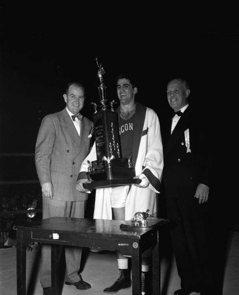 Vito Parisi, Wisconsin heavyweight champion, is holding the NCAA boxing tournament team championship trophy named for John Walsh. At left is Badger boxing coach John Walsh.
