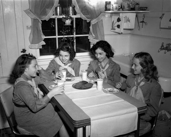 Four Girl Scouts enjoy a snack after delivering Girl Scout cookies, Nancy Reis (Highlands-Mendota Beach School), daughter of Mr. and Mrs. Joseph Reis, Virginia Grosse (Troop 110), daughter of Mr. and Mrs. Raymond Grosse, Eva Barash (Washington School), daughter of Mr. and Mrs. A.M. Barash, and Sandra Kneebone (Franklin School), daughter of Mr. and Mrs. M.J. Kneebone. The first Madison cookie sale was in 1928.