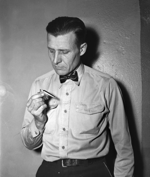 Police Officer Lester Shore, holding a "River Shiner" fishing lure, for which he holds a patent. It is a casting plug that has a metal lip and shaft and imitates the appearance and action of the shiner minnow, a natural fish food.