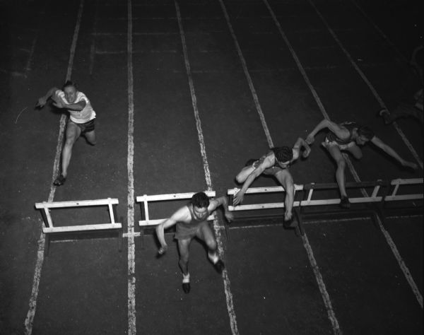 Elevated view of four hurdlers participating in Madison West High School Relay Carnival at the Field House. They are Dan Manneback, Kohler; Charles Starr, Richland Center; Dan Kuhn, West Bend, and Frank Loureckovich, Milwaukee Solomon Juneau.