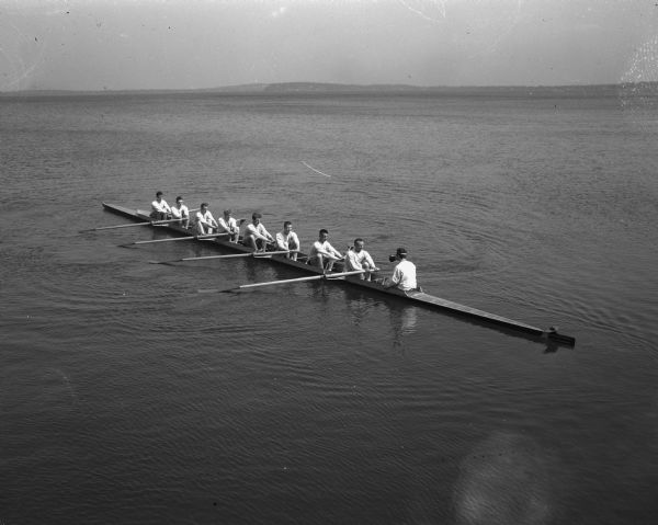 The University of Wisconsin varsity crew on Lake Mendota in its new pressed plywood racing shell, the <i>Mendota</i>, which was christened just before this photograph was taken.  The Mendota is believed to be the first shell constructed in the middle-west.  The varsity boat crew, left to right, is: Frank Harris, bow; Ralph Falconer, 2; Donald Peterson, 3; Gordon Grimstad, 4; Leroy Jensen, 5; willaim Sachse, 6; Richard Tipple, 7; Floyd Nixon, stroke; and Carlyle Fay, Coxswain.
