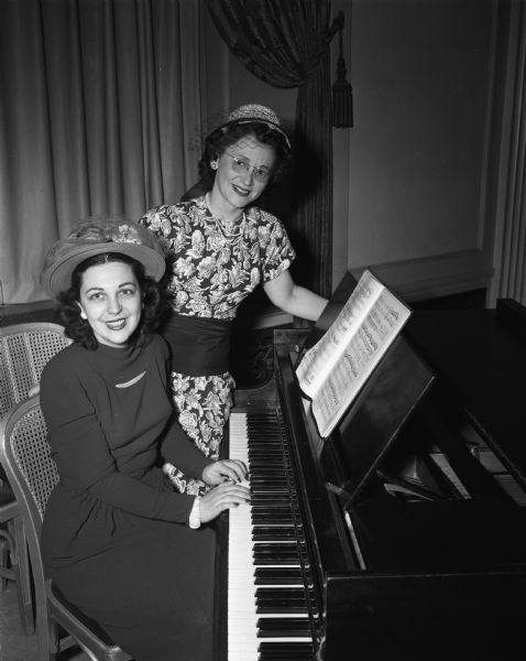 Two members of the Madison chapter of Hadassah at the first annual donor luncheon at the Hotel Loraine. Pictured is Mrs. E.M. (Anita) Weinshel seated at the piano and Mrs. David A. (Elizabeth) Woods standing. Mrs. Woods served as a captain of the Hadassah drive to raise money for the medical and youth centers in Palestine.