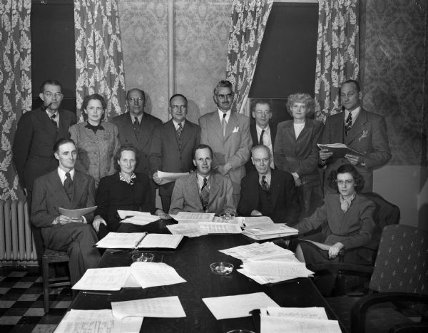 Board members of the East Side Youth Activities Council meeting to finalize their budget request to the Community Chest. Standing left to right: R.F. Stumpf, secretary of Madison Gas and Electric Company; Margaret F. Murphy, state banking commission; Ira Fuller, West High School; Peter C. Lynaugh, city council representative; John Gallaway, Oscar Mayer Co.; Fred Donner, Gisholt employe and CIO Council representative; Mrs. Frederick J. Meyer, housewife; Robert Carnes, director of East Side Council. Seated left to right: Selwyn R. Tuttle and Margaret Fosse, council board members; Francis F. Bowman, Jr., budget committee chairman; Marshall Browne, council board member and Phoebee Hayes, A.F. of L. representative. The Activities Council, 2425 Atwood Avenue, stimulates both youth and adult programs and coordinates programs of agencies on the East Side.