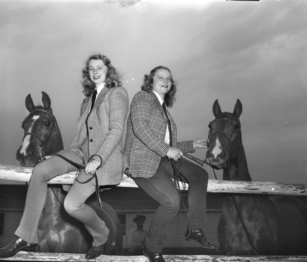 Two University of Wisconsin Hoofers' Club members who will ride in the annual horse show are shown sitting on a fence holding the reins of their horses. Pictured are Patricia Jane Ewell (left) and Nancy Tetzlaff (right).