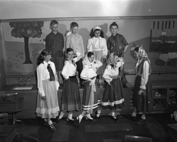 Nine students from Marquette School representing early Wisconsin settlers in Russian, Polish, and Czechoslovakian ethnic costumes performing in the school pageant celebrating Wisconsin's centennial. Pictured from left to right are: in the front row, Jane Rodenfels, Jane McGregor, Dyanne Wedlake, Shirley Femrite, and Joyce Jana; and in the second row, Carl Hubbard; Oliver Olson, Sandra Spraetz, and James Schantz.
