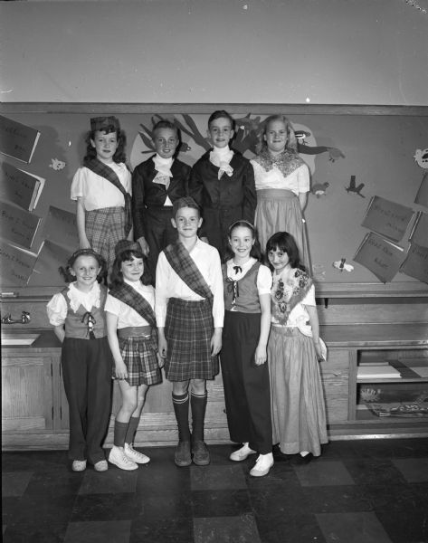 Nine students from Marquette School representing early Wisconsin settlers in British Isles costumes performing in the school pageant celebrating Wisconsin's centennial. Pictured left to right are: in the front row, Marilyn Strand; Mavis Thompson; Terry Le Gray; Carolyn Watzke; Delores Wyssbrod; and in the second row Loyce Capps; Kenneth Pollack; Arland Kuester; and Barbara Stoflet.