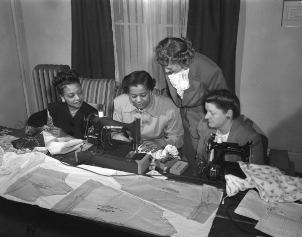 Four women sewing a 'sleeping garment' at the Blessed Martin House, 746 West Washington Avenue, an interracial and interfaith center sponsored by Madison Catholics, on its first anniversary.  Pictured from left to right are: Mrs. Howard C. (Mary E.) Cooper; Mrs. William (Lucille) Miller; Mrs. E.B.A. Sokolski; Mrs. Paul J. (Theresa) Uselmann.