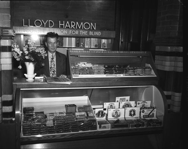Lloyd Harmon, from Belleville, who has been blind from birth, standing at the first concession stand to be erected in the Dane County Court House. The display cases and storage cabinets were installed by the adult blind division of the State Department of Public Welfare.