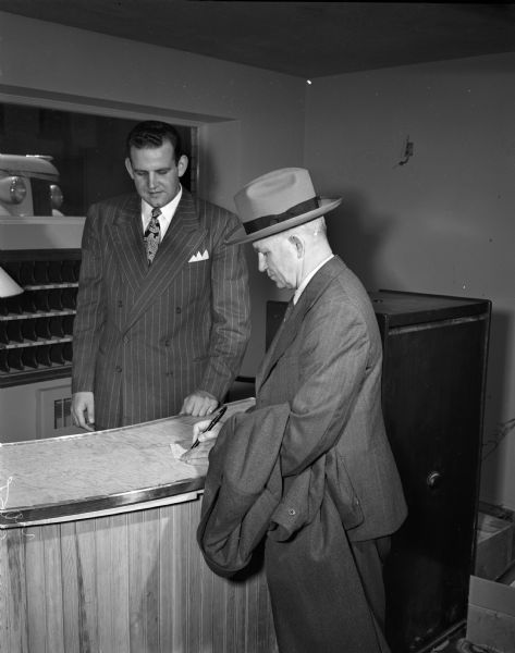 Edgewater Hotel manager, Austin Falkner, watches Dr. Donald Bowle register as the first guest at the hotel. Dr. Bowle is professor of the department of anatomy at the University of Manitoba, Winnipeg, Canada.