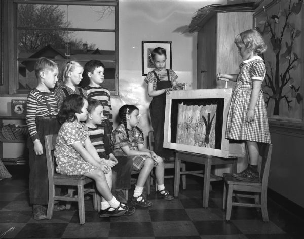 First grade students at Madison's Washington School used special activities to help build their vocabularies. In this photograph students are watching a "movie" they made. Shown unreeling the "film" are Dennis Anderson and Susan Goodrich. Watching are Jean Linde, Raymond Kieffer, and Maro Mills (seated) and Larry Lulling, Nancy Fries, and Douglas Kendall (standing). Mrs. Alice Wing is the class teacher.
