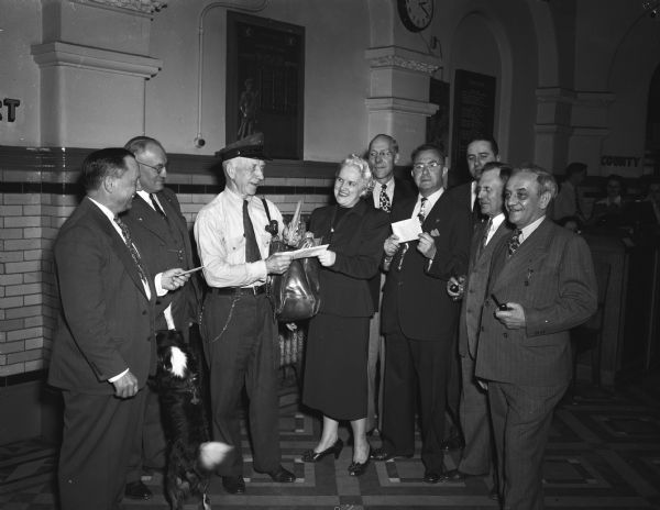 Retiring mail carrier, Mike Cawley, accepting an envelope containing a token of appreciation from Myrtle L. Hansen, clerk of circuit court at the Dane County courthouse. He had carried mail in Madison's old fourth ward for more than 30 years. Others in the picture are, left to right, are Austin N. Johnson, county clerk; County Judge, Fred M. Evans; Julius Kelley, county treasurer; Circuit Judge, Alvin C. Reis; Deputy District Attorney, William J. Coyne; George E. Rude, register of deeds; and Sheriff Edward A. Fischer.