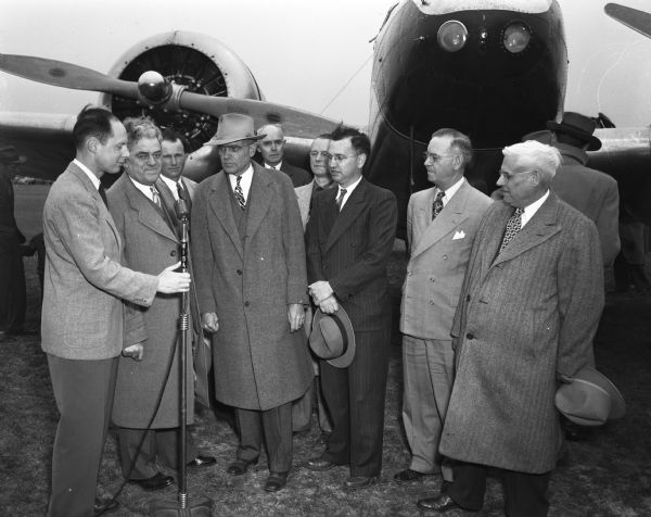 A group of men gathered in front of an airplane at the inauguration of Wisconsin Central Airline service to the Baraboo-Portage area. The men are local officials plus the president of the feeder airline. The plane in the picture is a Lockheed Electra, twin engine, nine passenger plane.