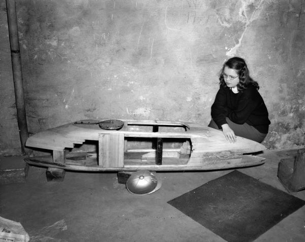 The Soap Box derby racer of Pierre Slightam is being guarded by the sister of the builder, Lucretia, daughter of Mrs. and Mrs. Francis Slightam. The picture is used to alert potential racing entrants to the availability of wheels and axles for their racing cars.