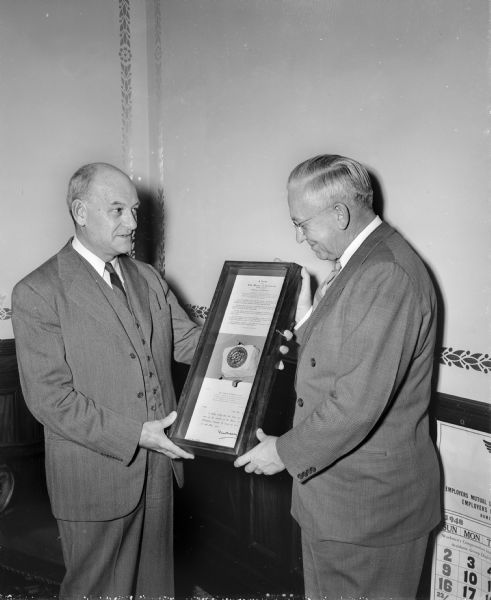 Pictured are Professor, Chester V. Easum, University of Wisconsin history department, at left, shown as he presented a case containing relics from the British house of commons, wrecked by German bombs in 1941, to Governor Oscar Rennebohm, at right. The case is a present from Charles Sumner Bird, president of the American and British Commonwealth association, and Eric Gordon Underwood, former aide of Winston Churchill, as a reminder of the ties between the two nations.