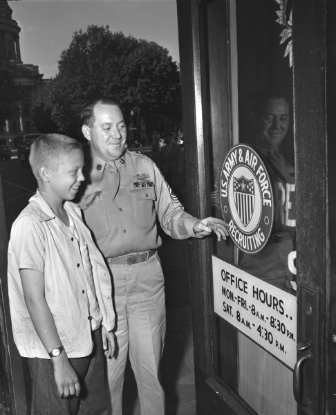Freddy Fleury, 14, of 210 N. Paterson Street, talks over plans for his 1948 Soap Box Derby racer with Master Sgt. Wilfred W. Wall at the U.S. Army & Air Force recruiting office at 215 Monona Avenue. (M.L. King Jr. Blvd.). A replica of the U.S. Army & Air Force Recruiting insignia will appear on either side of Freddy's racer. The Wisconsin State Capitol rotunda is in the background.