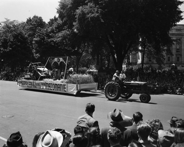 Wisconsin Centennial Parade near the Wisconsin State Capitol. The Mazomanie float is titled: "John F. Appleby Invents Twine Knotter in Mazomanie," and is pulled by a Farmall H tractor.