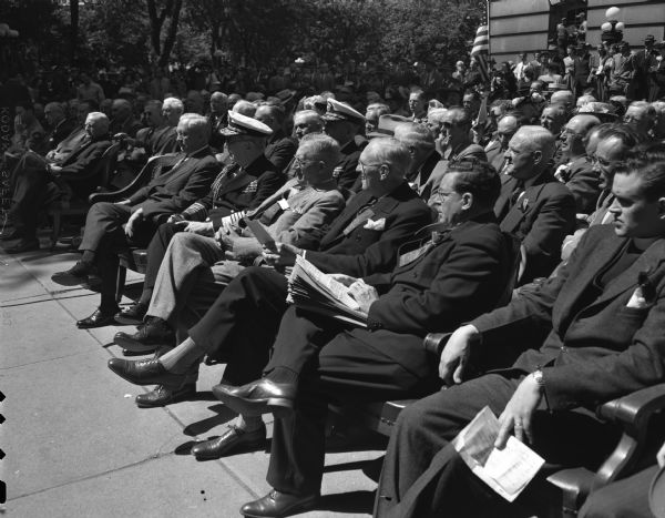 The viewing stand for the new voter ceremonies at the King Street entrance of the Wisconsin State Capitol. Admiral William D. Leahy (in uniform) is shown in the front row with Acting Governor Oscar Rennebohm to Leahy's right, and Ora Rice, chairman of the State Centennial Committee, to Leahy's left.