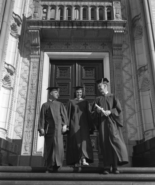 Three Edgewood High School graduates in cap and gown and holding diplomas. Standing before the front door of Edgewood High School, left to right are:  Tom Short, Peggy Snyder, and Jack Keegan.