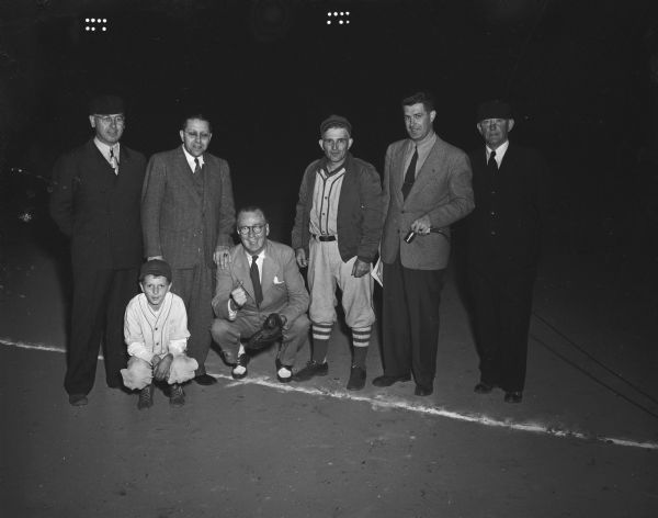 Group portrait of six men and one boy at a baseball game between the Penn Electrics and the Sauk City Red Sox marking the grand opening of Penn Park. Art Lentz introduced the dignitaries. 1,200 fans saw the Rev. Charles A. Puls, pastor of Luther Memorial church, throw the first pitch to Roundy Coughlin.