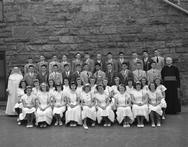 Group portrait of the eighth grade graduating class of St. Raphael Catholic School, 216 West Main Street, with a nun and a priest.