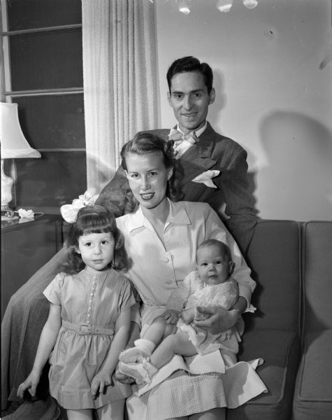 Portrait of Mr. and Mrs. Valbur Borger, Santiago, Chile, with their two daughters, pictured in the home of his parents, Mrs. and Mrs. George Borger, 3231 Tonyawatha Trail, Monona. Standing in front of her mother is Candice, and in her mother's lap, infant Valerie. Mr. Borger is with the foreign sales division of Universal Pictures.