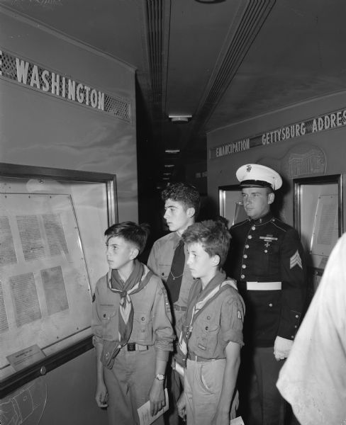 Sgt. James McCullough, Memphis, Tennessee, a marine veteran guarding the Freedom Train, points out Washington's Farewell Address to three Madison Boy Scouts. Pictured standing in front of Sgt. McCullough, are left to right, Bill Marsh, 224 West Sunset Court; Tom Smith, 314 West Sunset Court, and Jim Watts, 3807 Hammersley Road. The Freedom Train, parked on the tracks behind the Chicago, Milwaukee, St. Paul & Pacific Raiload station, 644 West Washington Avenue, is making a 3,300 mile tour of the nation, bringing 127 documents and relics of American history.