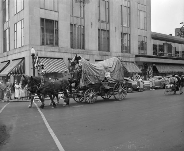 Sun Prairie Chamber of Commerce float (horse-drawn, covered wagon) in the Eagles annual parade, on East Mifflin Street.  Manchester's store, at the corner of Wisconsin Avenue and East Mifflin Street.