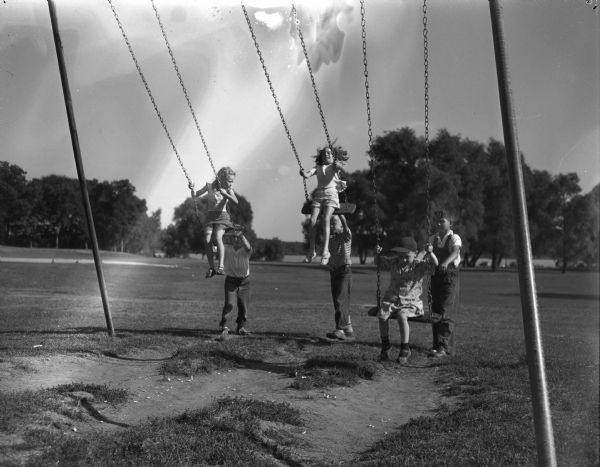 Playing on the swings at Wingra Park are James Bruce swinging Anne Meyers, Mike Cantwell swinging Peggy Aspinwall, and James Clark swinging Rene Burkhalter.