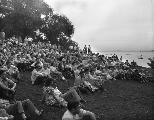 A crowd of students and townspeople seated on the grass at the Memorial Union terrace to hear a concert by the University of Wisconsin summer session band.