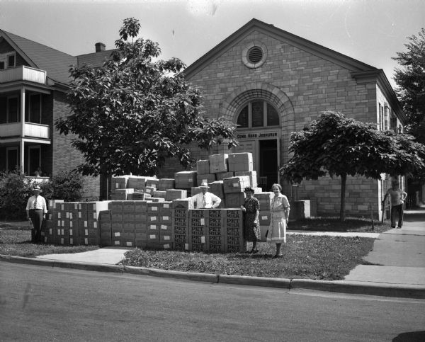 View from road of large stacks of boxes containing food and clothing on the lawn of Congregation Adas Jeshurun temple at the corner of Mound and Murray Streets. The supplies were collected by seven Jewish women's organizations for distribution in overseas displaced persons camps.
Shown from left are Israel Sweet, Sam Mead, Mrs. S.B. (Cecile) Schein, and Mrs. Israel (Esther) Sweet.