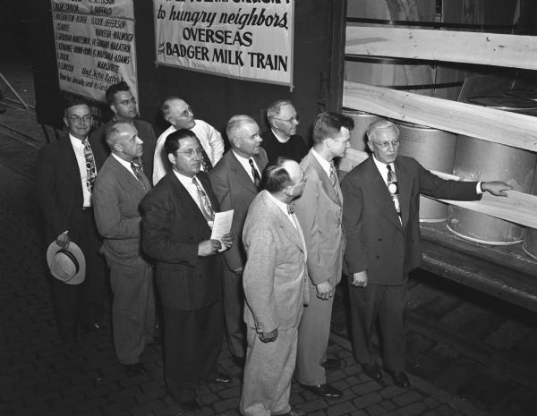 Group portrait of Governor Rennebohm with nine men looking at a boxcar of the CROP (Christian Rural Overseas Program) train. The nine-carload train contains Wisconsin foods destined for post-war refugees in Europe and Asia. Pictured left to right: Rev. F. Schwertfeger, Claire Jackson, Rev. W.C.F. Hayes, Prof. W.W. Clark, Rev. Erick Lenz, Rev. M.A. Sorenson, Rev. George Heusler, Prof. Noble, Robert Lewis and Governor Rennebohm.
