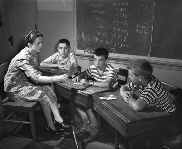 Participants in a large-scale hearing clinic held at Washington School in Madison and sponsored by the University of Wisconsin departments of speech and education with the cooperation of the state bureau for handicapped children. Three children are playing a game with speech therapist, Helen Bruce.