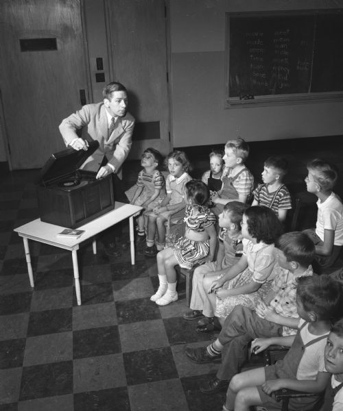 Participants in a large-scale hearing clinic held at Washington School in Madison and sponsored by the University of Wisconsin departments of speech and education with the cooperation of the state bureau for handicapped children. Roger Maas, clinic director, is shown leading children in a nursery song, a wonderful way to help children with a language disability.