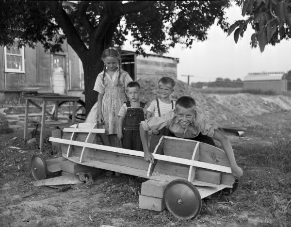 Jimmy Christiansen is shown posing with the body of his derby car while three friends observe. Left to right: Florence Brown, John Brown, Gary Sachs, and Jimmy Christiansen, who will compete in the Soap Box Derby.