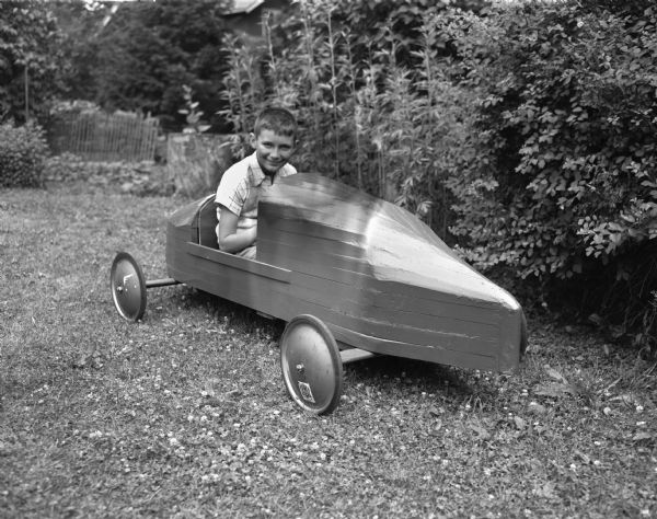 Soap Box Derby racer Bobby Holmes seated in car outdoors on grass.