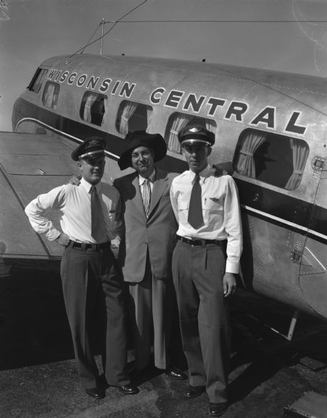 Two pilots with a guest posed in front of a Wisconsin Central airliner.
