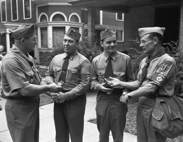 Two members of the Scouting committee are presented with emergency service emblems while on duty at the Soap Box Derby; left to right: F. F. Malcomson, corps director, presenting an emblem to Edwin E. Carter, Turner scouting committee members, and Walter W. Kopp, chairman of the Turner scouting committee, receiving his emblem from D. Stranger, director of emergency service for the Turner Society.