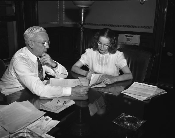 Governor Oscar Rennebohm seated at a table with an unidentified young woman. Photograph taken for Mr. Drummond, Appleton, of Employers Mutual of Wausau.