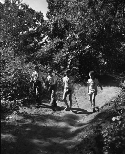 Four campers hike along a trail at Camp Wakanda, left to right: Raymond Nagel, son of Mr. and Mrs. Henry Nagel, 2810 Dahl Street, Carl Fosmark, son of Dr. and Mrs. Carl Fosmark, 602 South Thornton Street, James Gillies, son of Mr. and Mrs. P.H. Gillies, Marlborough Heights, and Richard Schuller, son of Mr. and Mrs. Charles Schuller, 4201 Mandan Crescent.