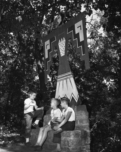 Three campers under the Camp Wakanda emblem, the Giant Eagle, at the camp's council ring are, left to right: Robert Hesse, son of Mr. and Mrs. Robert Hesse, 2218 Eaton Ridge, Peter Cash, son of Mr. and Mrs. James Cash, 523 North Carroll Street, and Fred Malcolmson, son of Mr. and Mrs. F.F. Malcolmson, 1028 East Washington Avenue.
