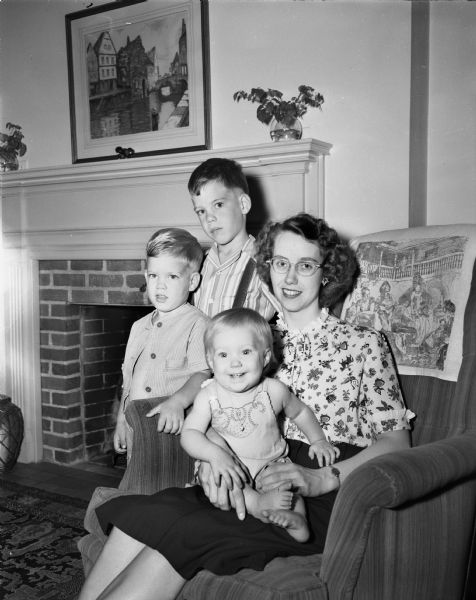 Mrs. Edward W. (Sally Jean) Hird, Wapakoneta, Ohio, seated in chair with children Jack, Bill, and Sally Jean. The family is visiting her parents, Mrs. and Mrs. L.L. Oeland, 1709 Hoyt Street.