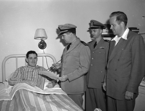Leroy L. Dalton,(in a hosptial bed at left,)shown receiving the United States Navy Air Medal for meritious achievement during his  fifth mission as a gunner or bomber during action in the Pacific in 1944. Awarding the medal are left to right: Lieut. Commander Raymond J. McCue, Lieut. Commander G. L. Block, and John Jamieson, public relations officier of the Madison naval reserve. Mr. Dalton was discharged from the navy March 3, 1948, and was enrolled at the University of Wisconsin when he contracted tuberculosis. He is a patient at the Lake View sanatorium.